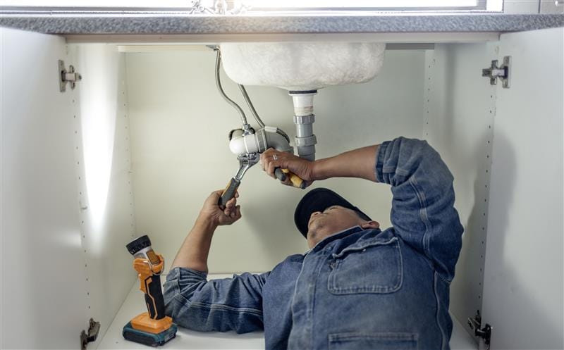 Plumber repairing pipes beneath a bathroom sink in Oviedo