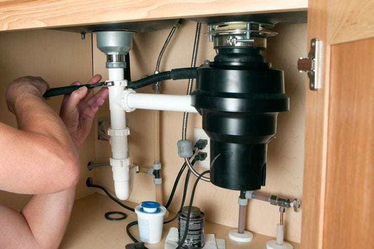 Plumber installing a garbage disposal beneath a kitchen sink in Oviedo