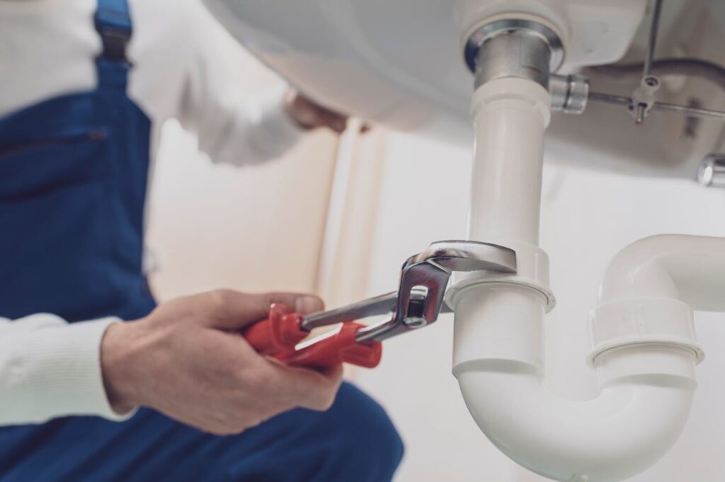 Plumber repairing a white drain pipe beneath a sink in Oviedo